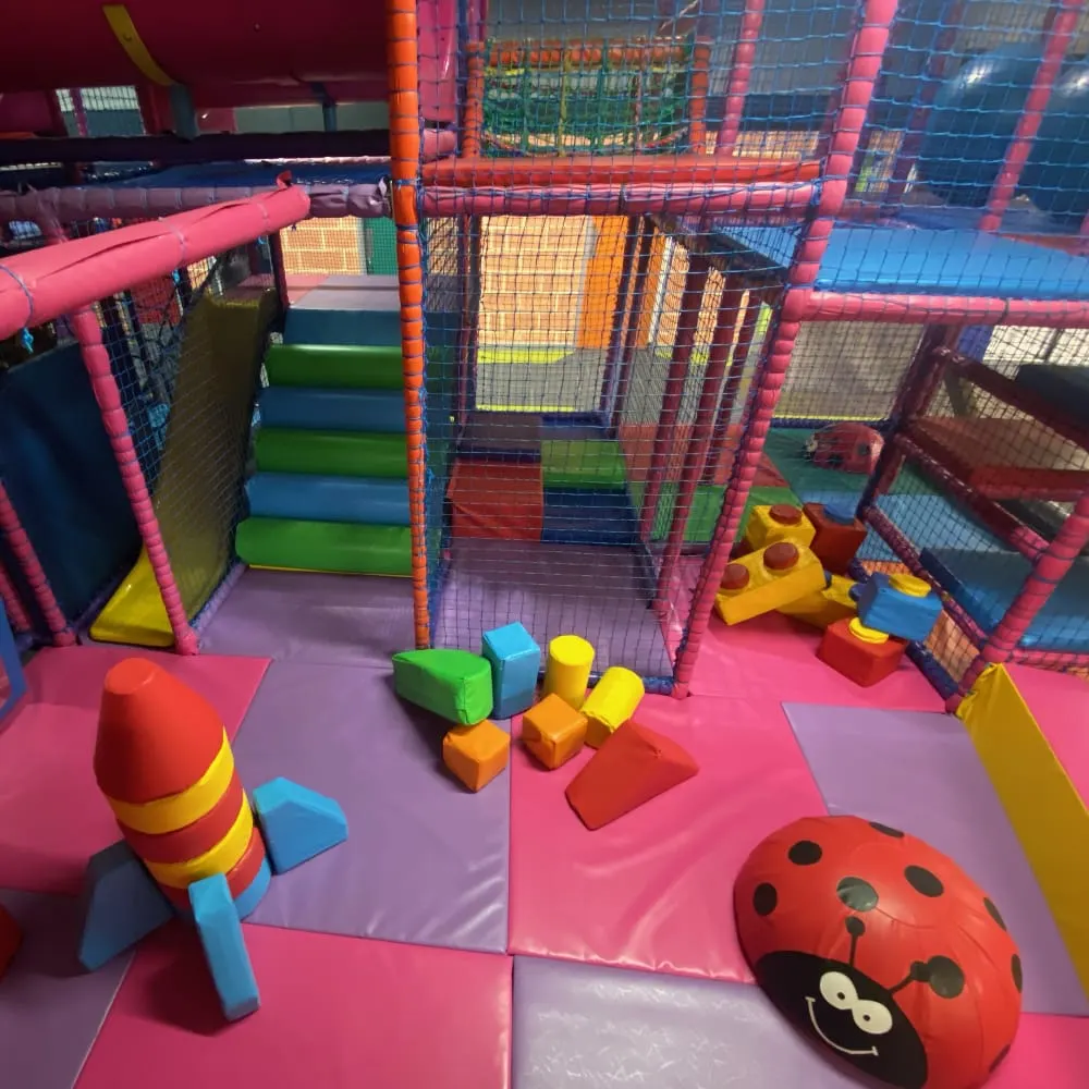 Colourful indoor play structure with pink padded flooring, foam toys and climbing equipment for young children.