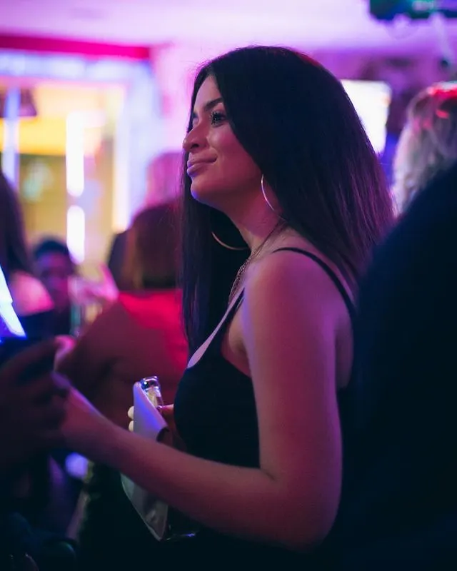 Woman enjoying a night out in a vibrant purple-lit nightclub with other guests around her.