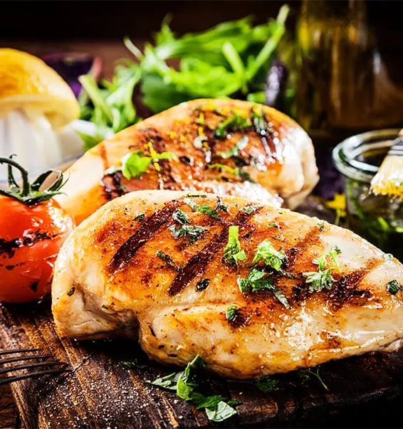 Grilled chicken breasts with herbs and char marks, served with fresh salad, tomato and lemon.
