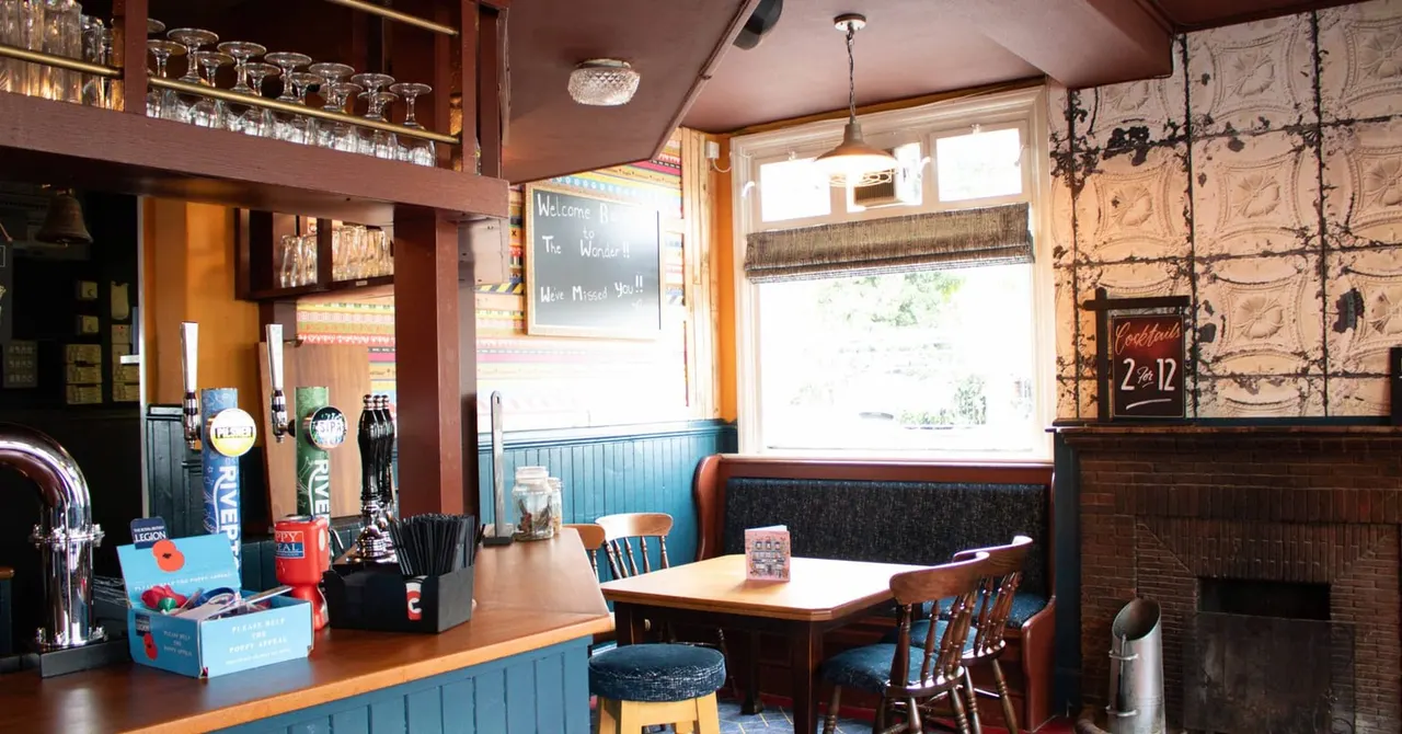 Bar and seating area with wooden furniture, beer taps, shelving with glassware, and a welcome message on a chalkboard.