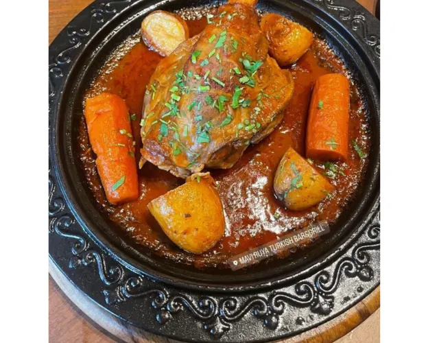 Meat stew with carrots and potatoes in rich brown sauce, served in a decorative cast iron pot.