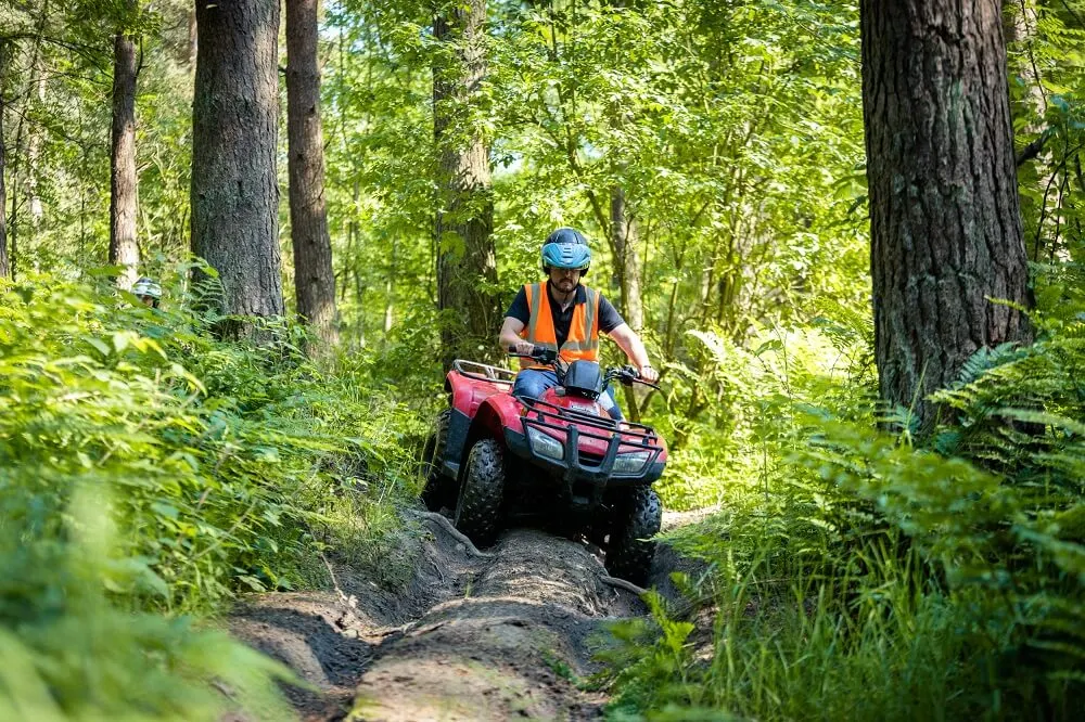 Person riding a red quad bike on a rocky woodland trail wearing a blue helmet and orange safety vest.