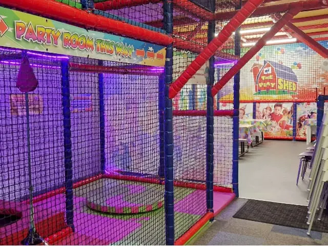 Colourful indoor play area with purple-netting enclosed structures and red support beams in a children's entertainment venue.