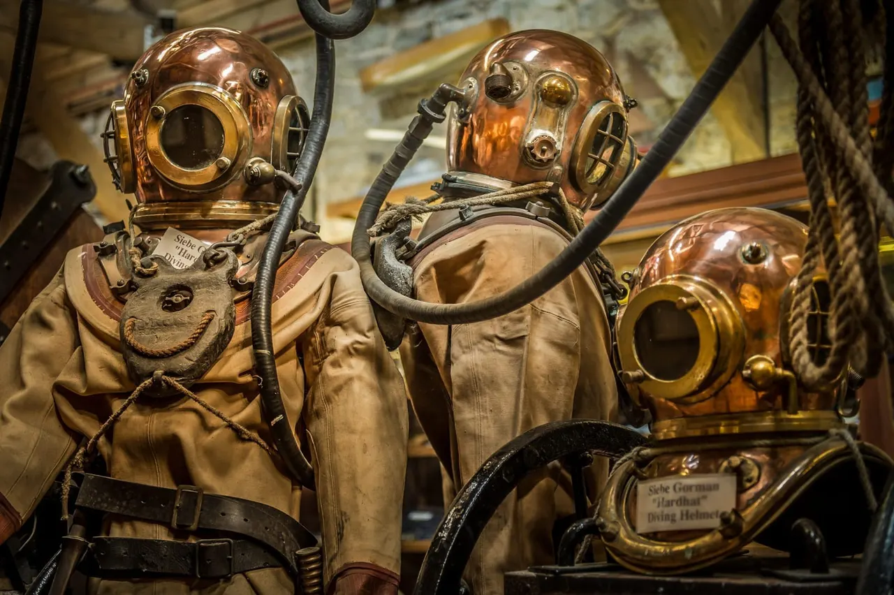 Vintage copper and brass diving helmets with air hoses and canvas suits displayed in a museum setting.