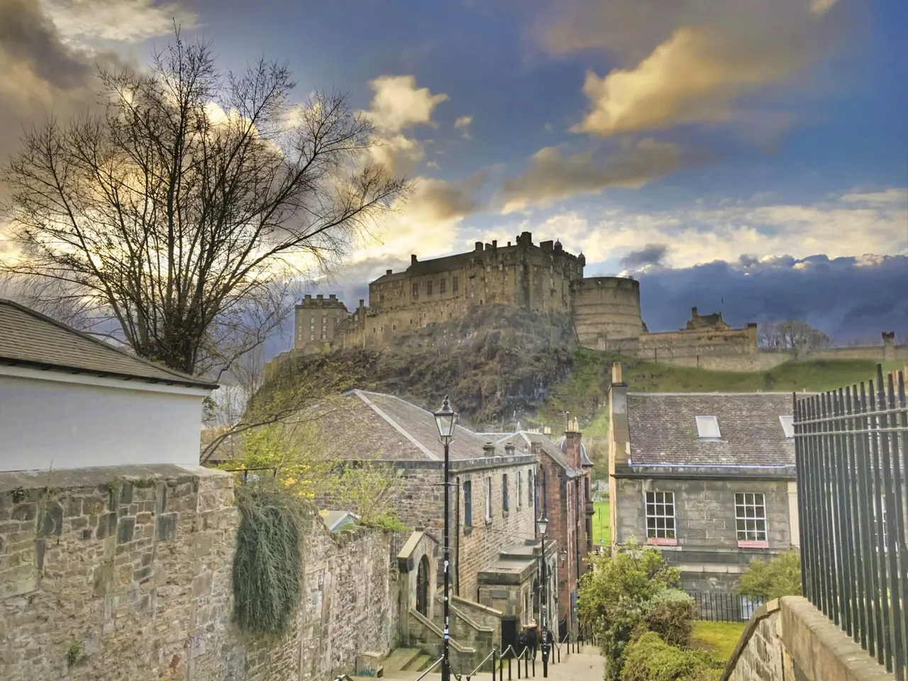 View down a cobbled street towards Edinburgh Castle perched on a volcanic rock, with historic stone buildings below.