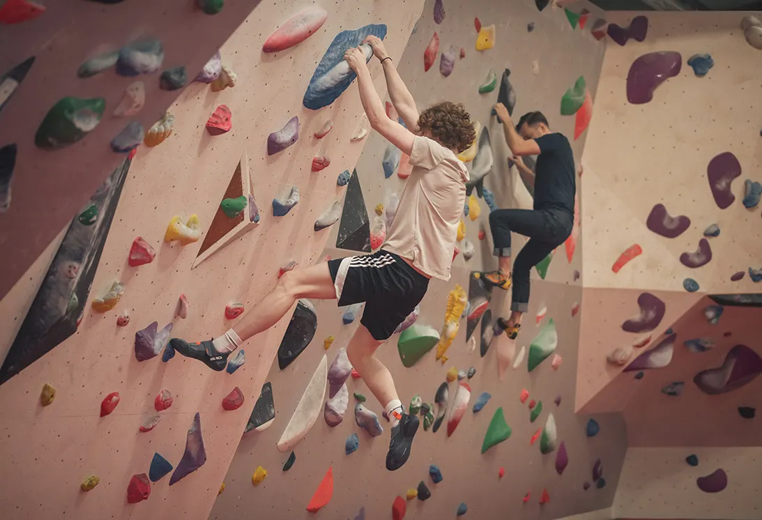 Children climbing coloured handholds on indoor climbing walls at an activity centre.
