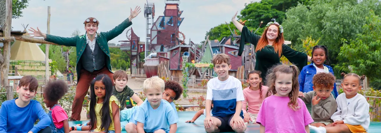 Group of children with an adult entertainer posing in front of a themed adventure playground structure at a leisure venue.