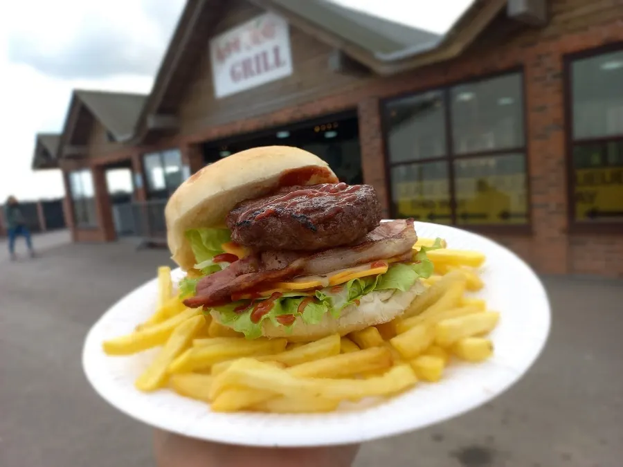 Stacked burger with bacon and lettuce served with chips, held up in front of a brick building.