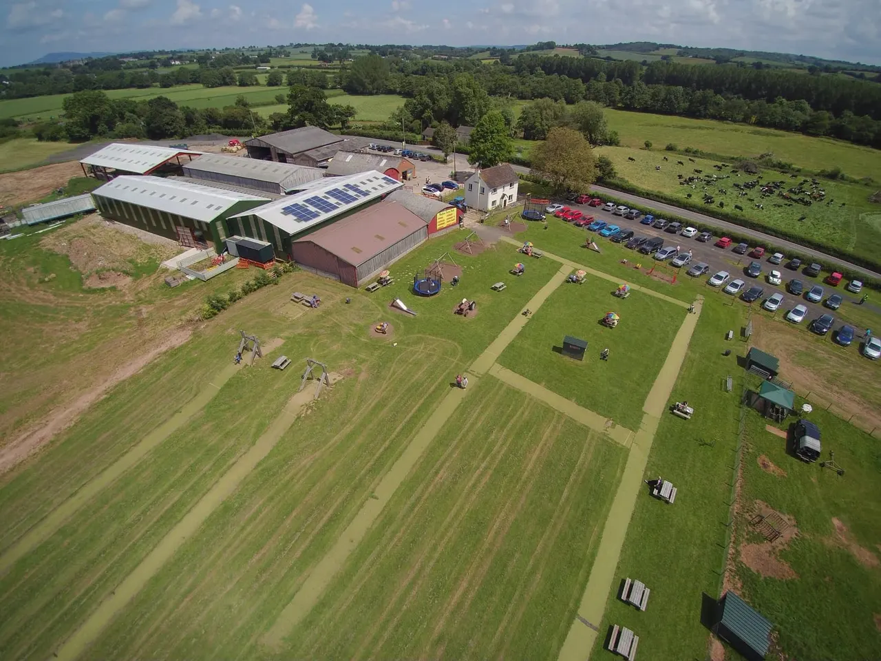 Aerial view of a farm park with play equipment, visitor facilities, car park and surrounding agricultural land.
