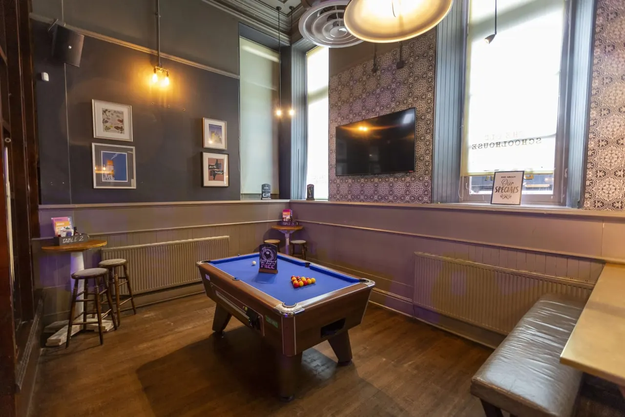 Pool table with blue baize in an upmarket games room with purple and cream wall panelling, bar stools, framed artwork, and a wall-mounted television.