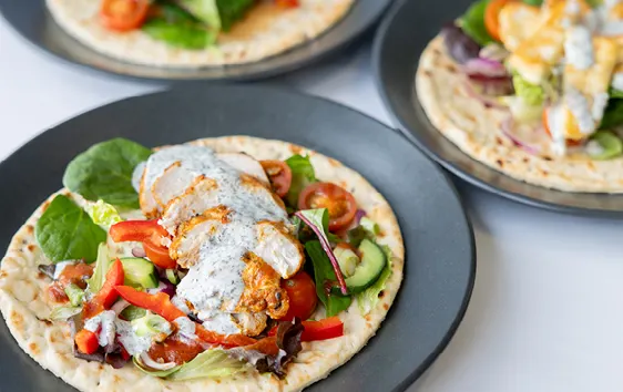 Grilled meat wraps with fresh vegetables and white sauce on flatbread, served on dark plates.