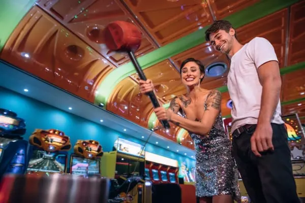 Two people playing whack-a-mole at a colourful arcade with gaming machines in the background.
