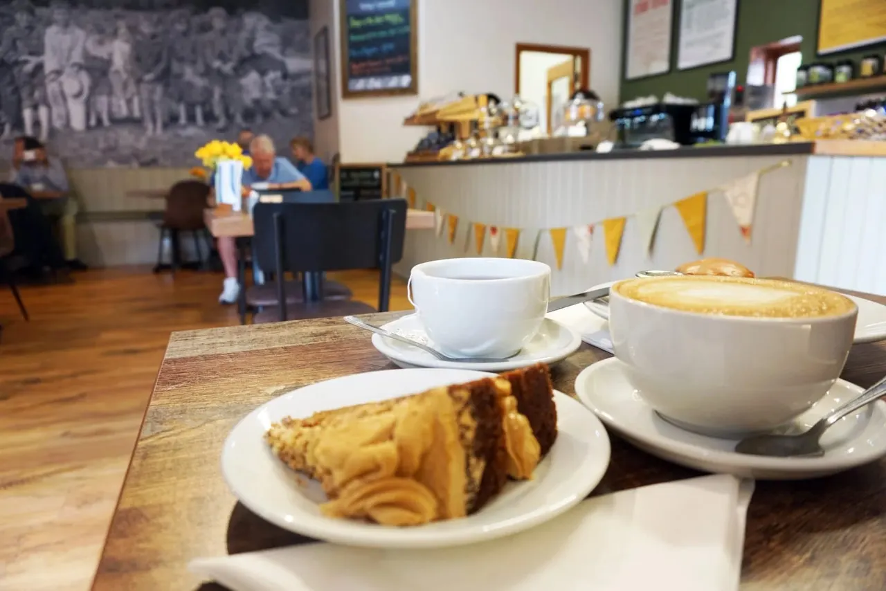 Coffee and cake served at a café table, with customers seated in the background.