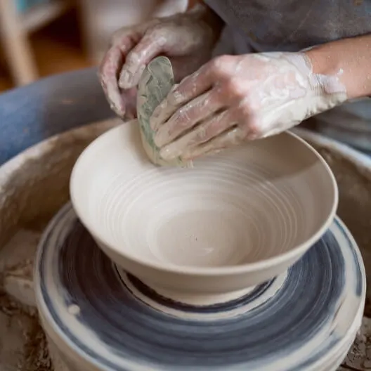 Person shaping wet clay on a pottery wheel during a ceramics workshop.