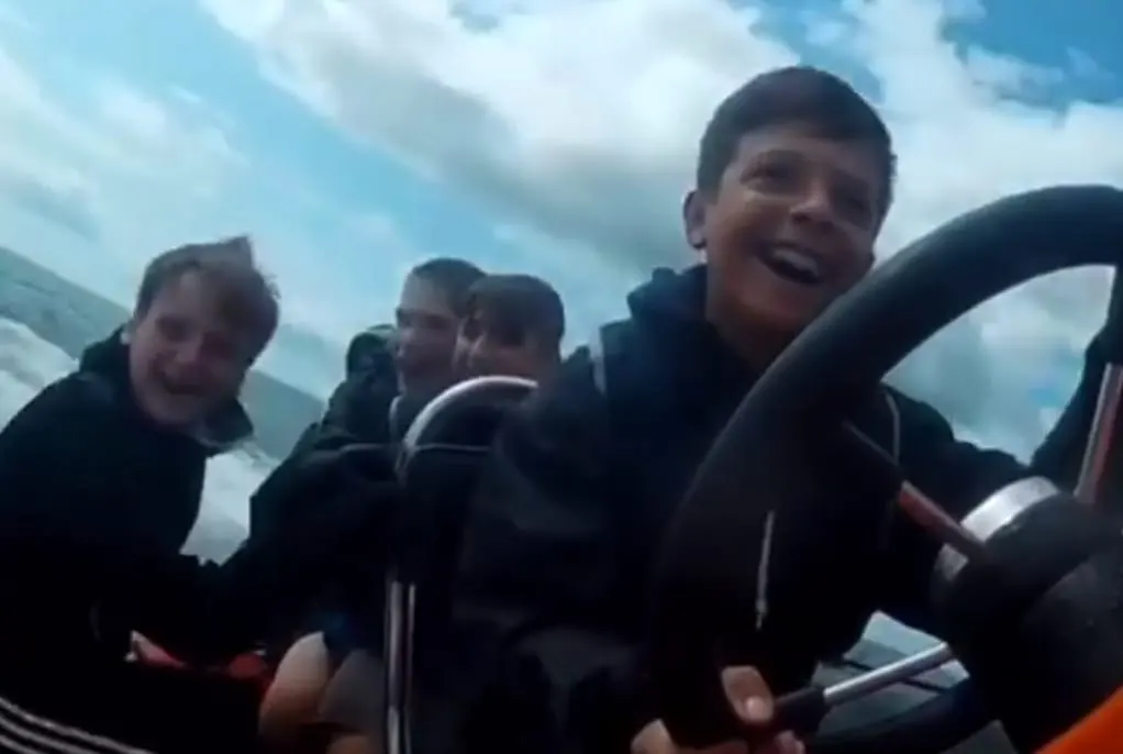 Children on a speedboat ride on water with cloudy sky above.