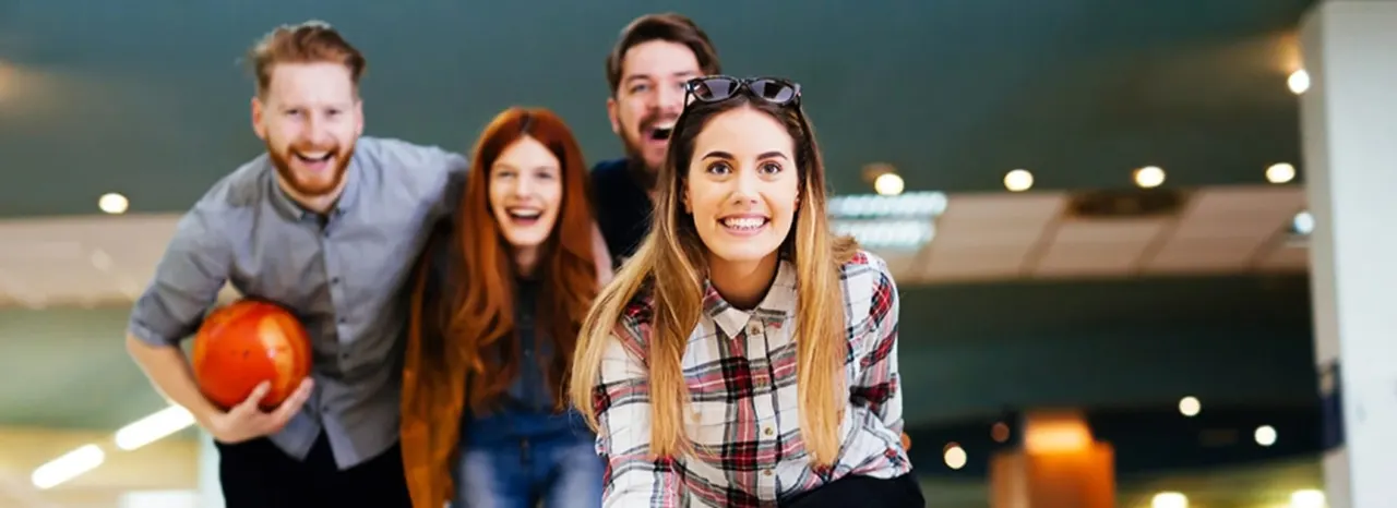 Four young adults enjoying themselves at a bowling alley, one holding a red bowling ball.
