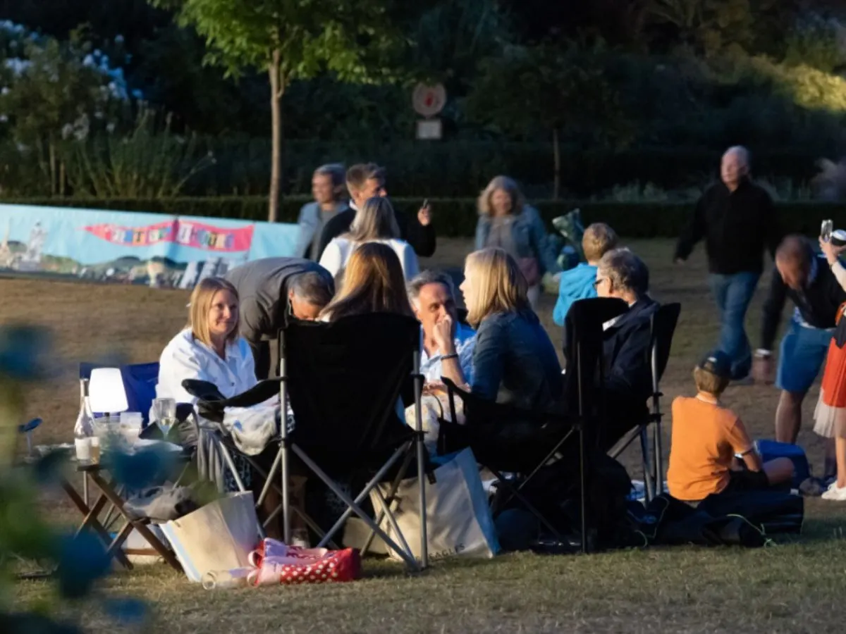A group of adults and children seated on camp chairs in an open-air garden setting during an evening event.