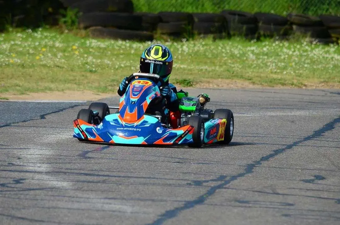 A driver in a blue and orange racing kart with green accents navigates a track corner.