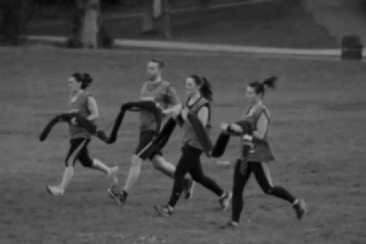 Four women running together on an outdoor track in black and white archival footage.