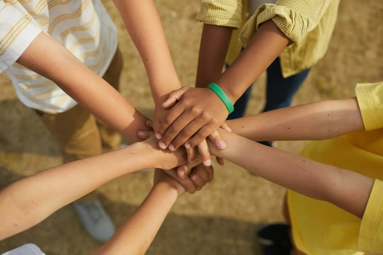 Group of children placing hands together in a team gesture outdoors.