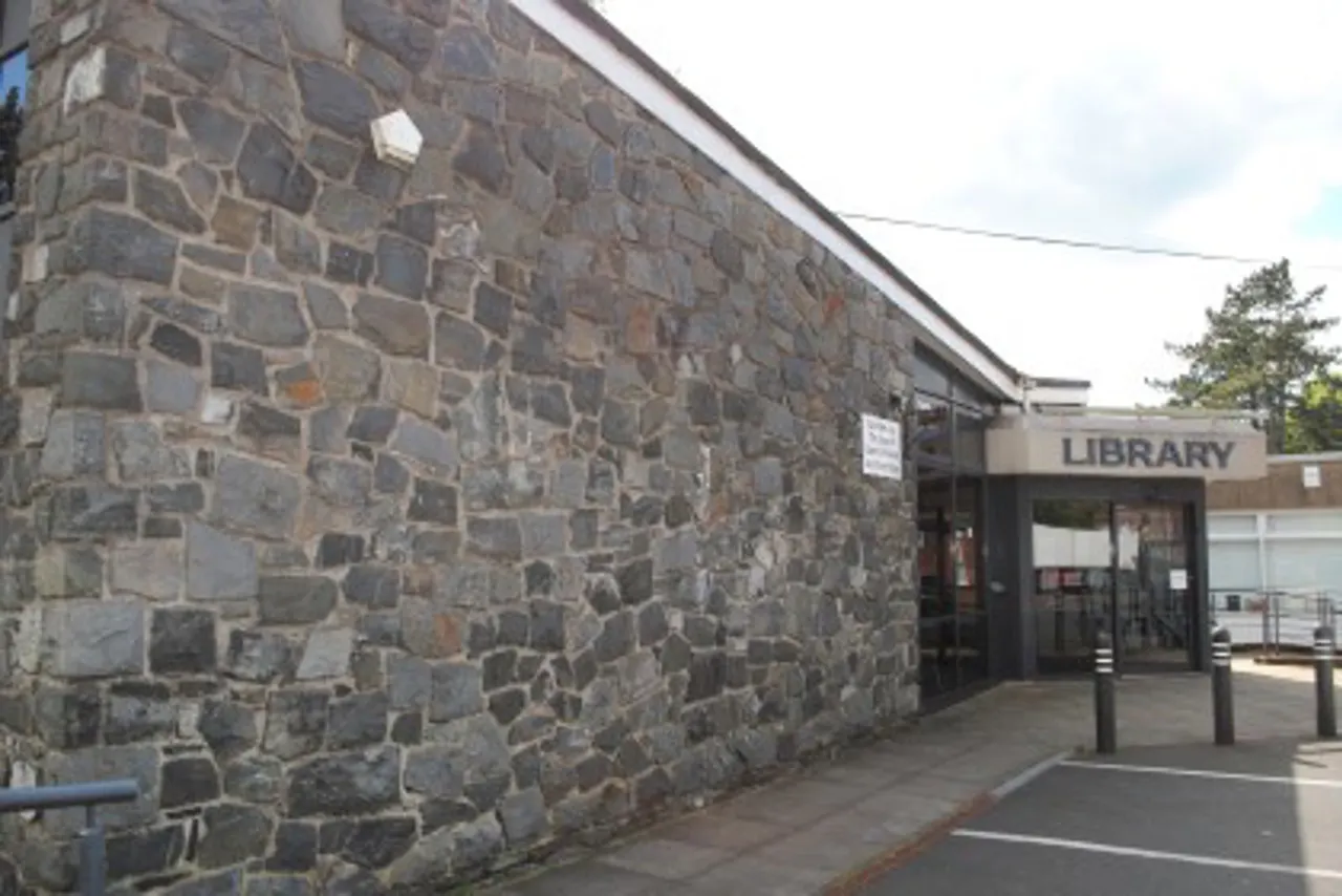Exterior of a stone-built library building with modern entrance, showing rough stone wall and signage.