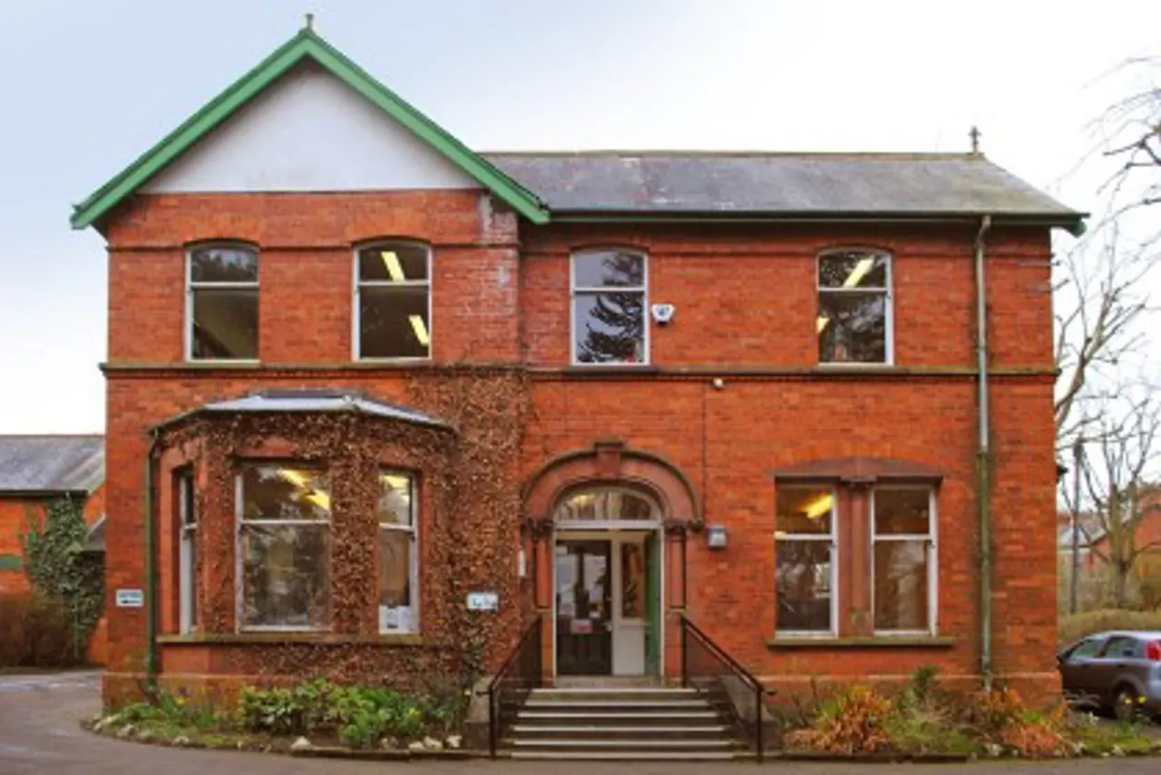 Victorian red-brick building with green roof trim, arched entrance, and lit windows at dusk.