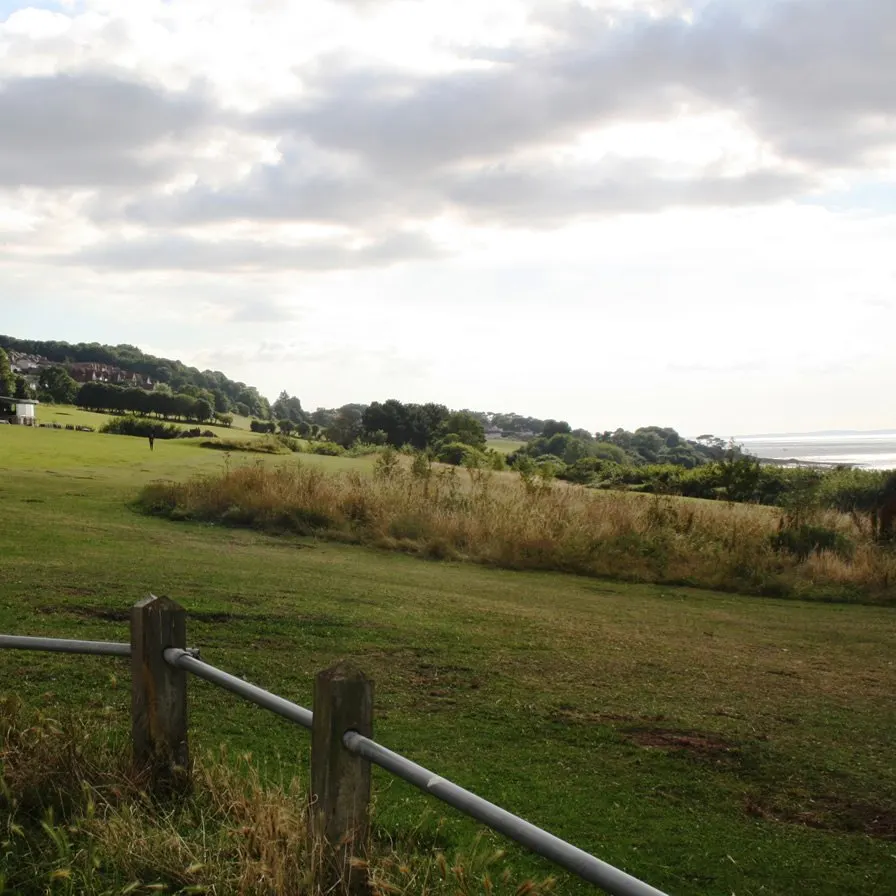 Rolling countryside with green fields, hedgerows and distant water views visible beyond wooded hills.