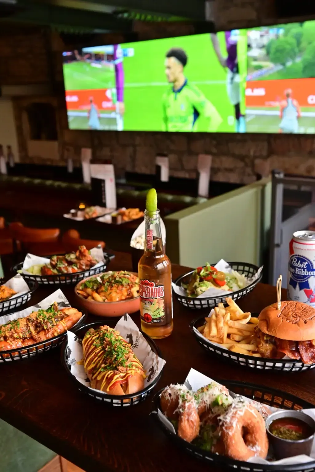 Table of food and drinks with a football match displayed on a screen above.