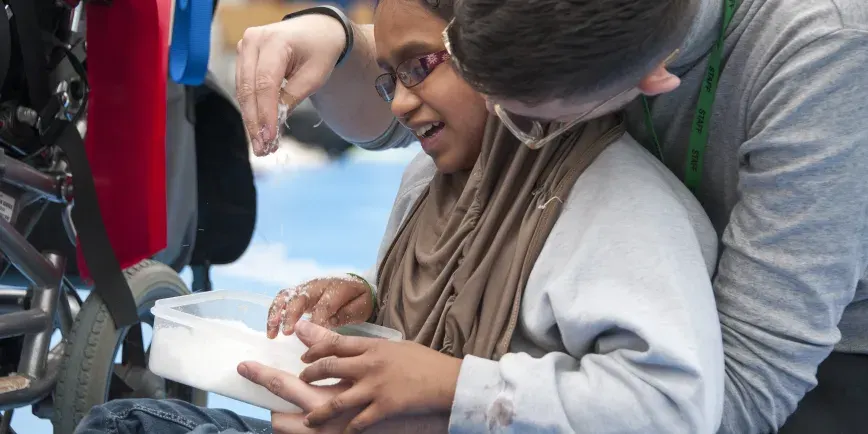 A young person wearing glasses holds a container while examining a starfish during a hands-on marine activity outdoors.