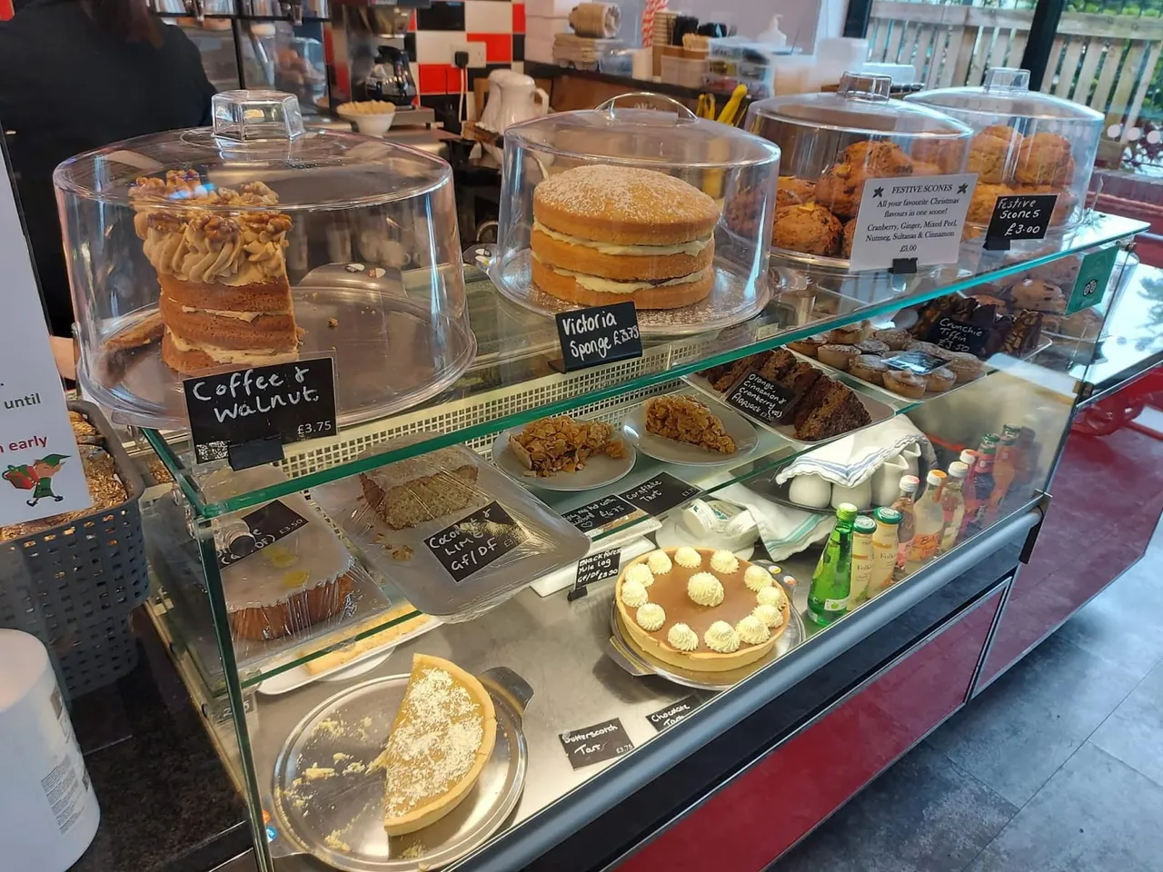 Bakery display case with cakes, sponges, biscuits and pastries in glass domes and on plates.
