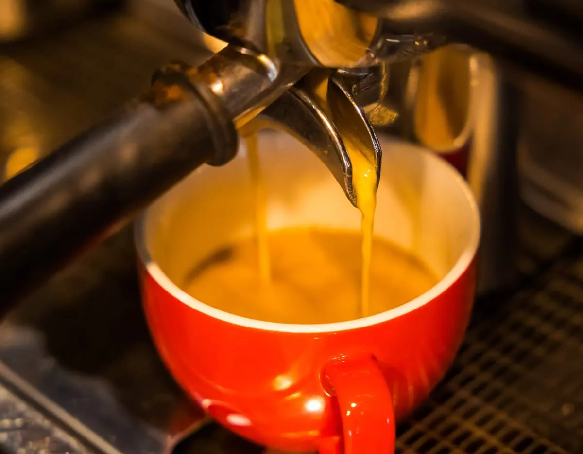 Espresso machine pouring golden espresso into a red cup.