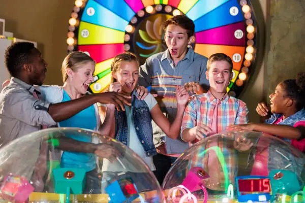 A group of six people playing an interactive game at a colourful illuminated arcade machine with a large spinning wheel backdrop.