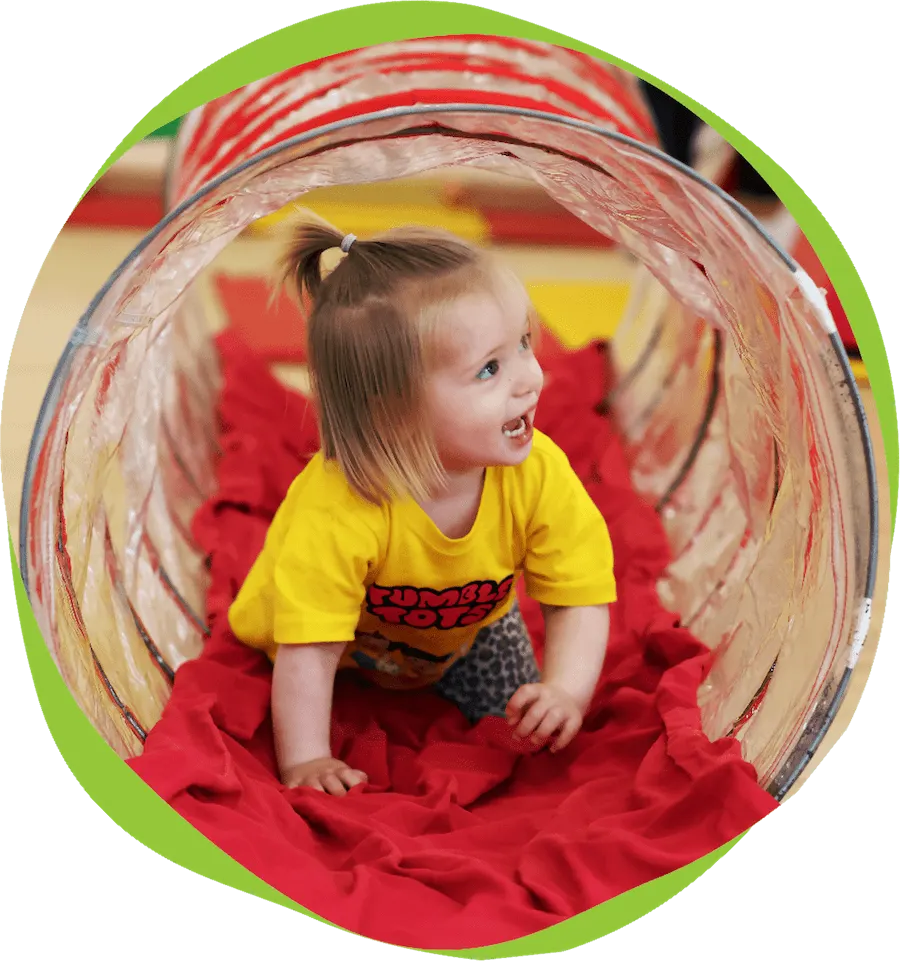 Young child crawling through a red fabric play tunnel at an indoor soft play facility.