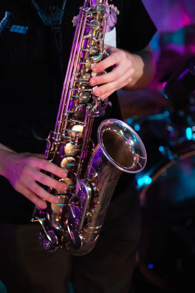Musician playing saxophone under purple and blue stage lighting during a performance.