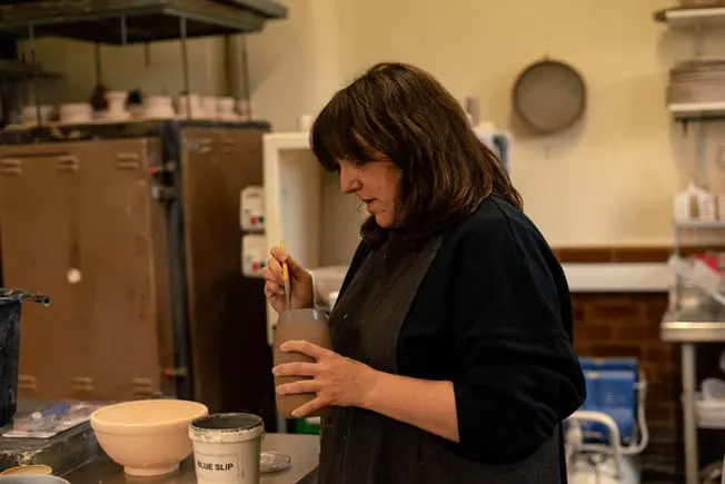 Woman working at a pottery wheel in a studio, shaping clay.