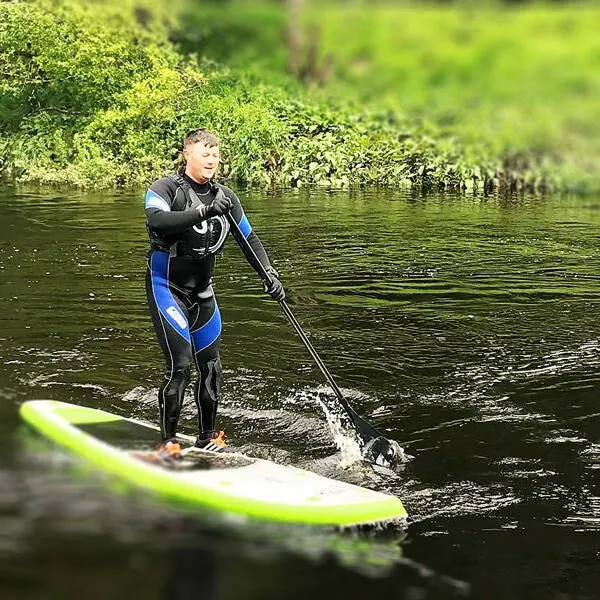 Person in blue kayak paddling through narrow waterway lined with lush green vegetation.