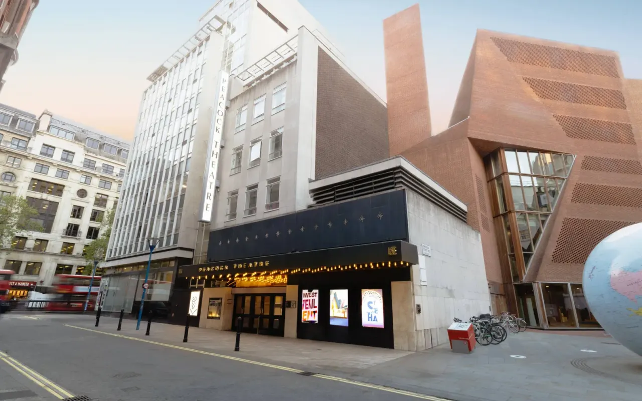 Theatre building with black frontage and illuminated signage on a central London street, surrounded by modern and period architecture.