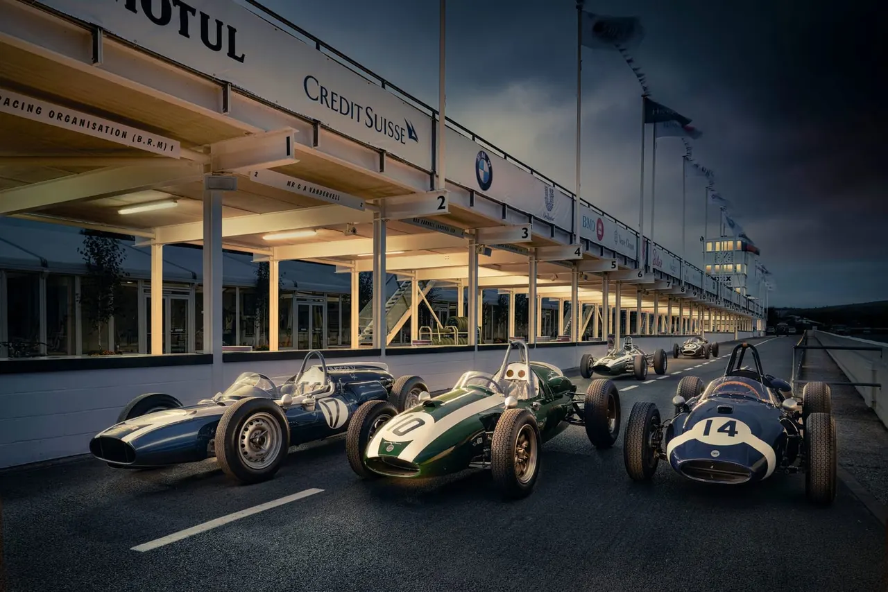 Classic racing cars parked at the paddock entrance of a historic motorsports venue at dusk.