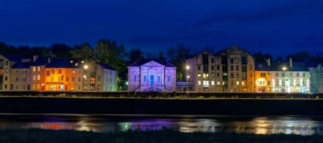 Historic waterfront buildings illuminated at dusk, reflecting in the river below.
