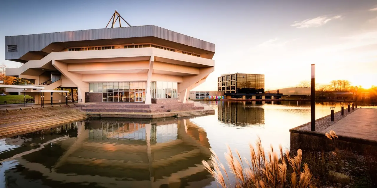 Modern waterside building with distinctive curved architecture reflected in calm canal water at sunset.