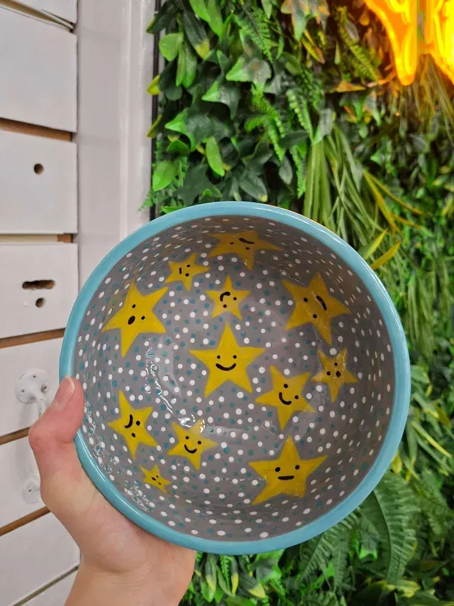Hand holding a blue colander with smiling star design against green foliage backdrop.