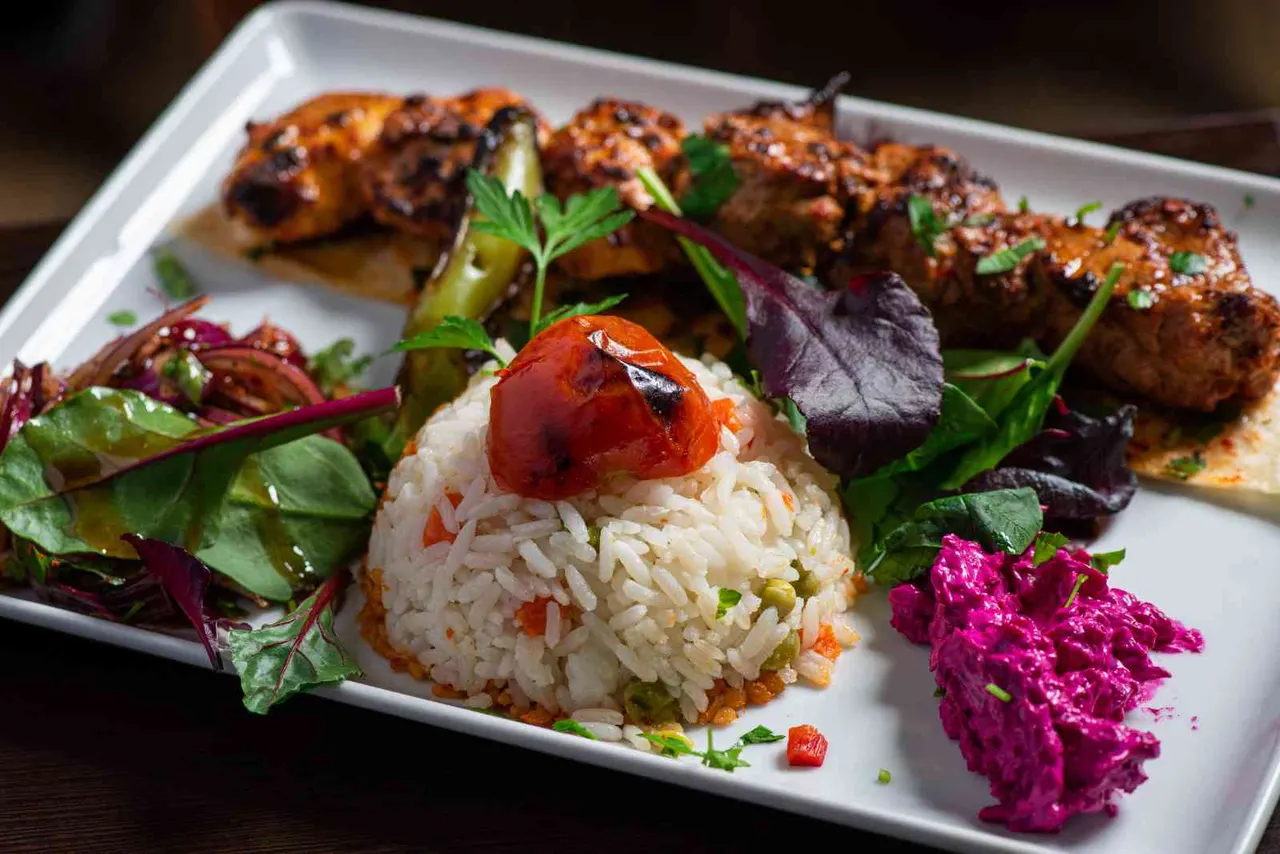 Grilled meatballs and rice cakes with roasted peppers, beetroot salad and fresh herbs on a white platter.