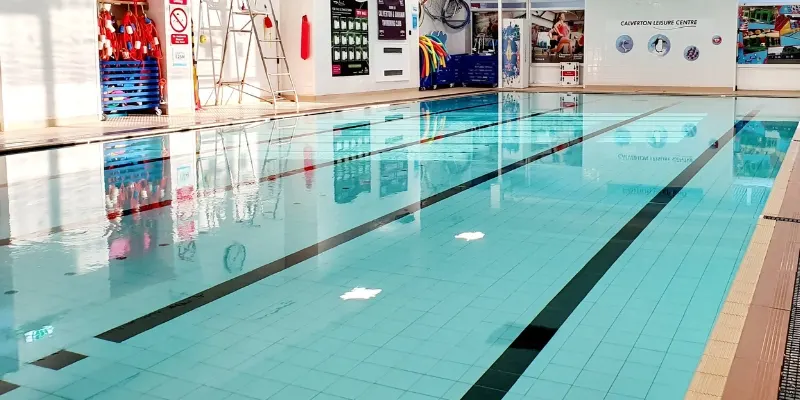 Empty indoor swimming pool with lane dividers and equipment stored along the poolside.