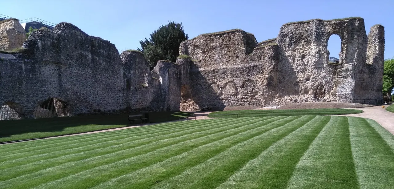 Striped lawn in front of extensive stone ruins of a medieval abbey under clear blue sky.