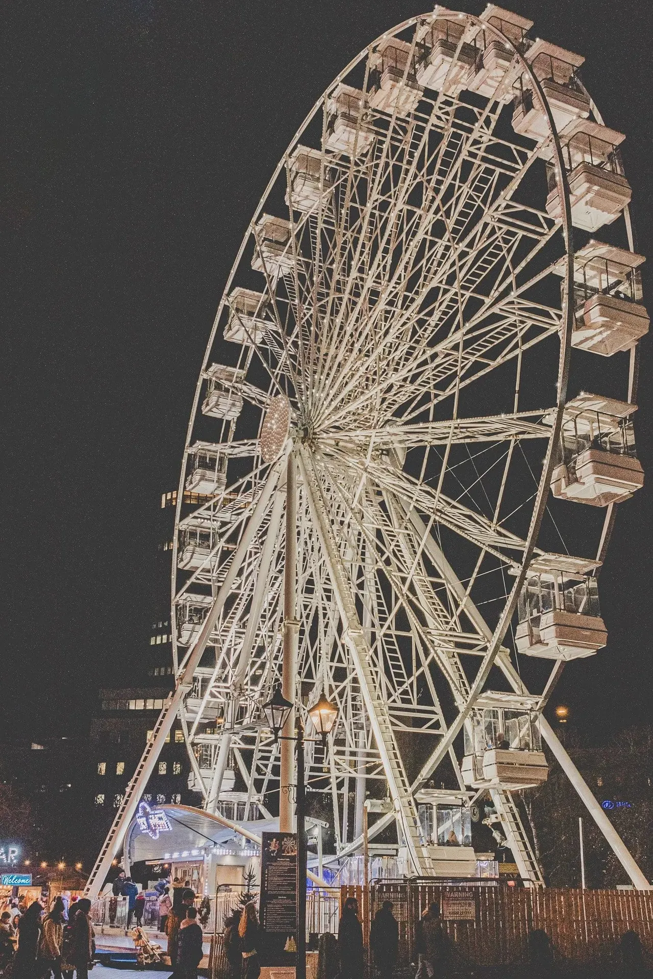 Illuminated Ferris wheel at night with visitors gathered at its base during winter festivities.