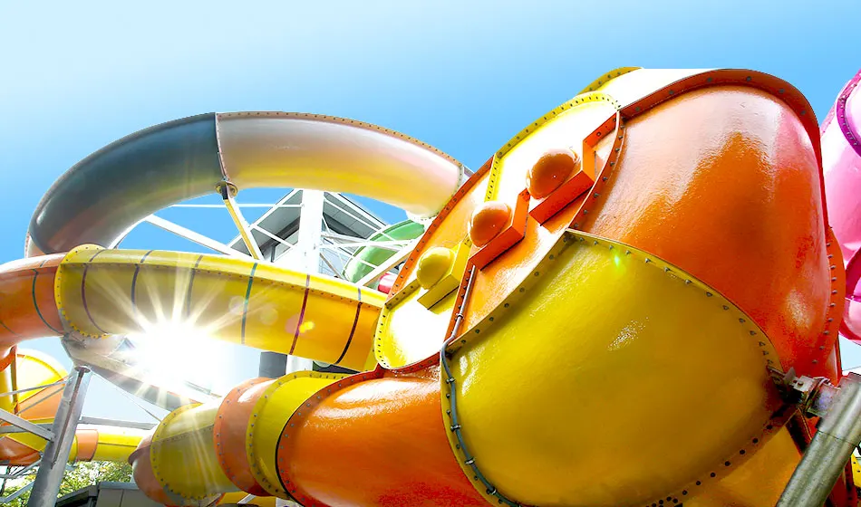 Colourful water slide tubes in bright yellow, orange and red against a clear blue sky at a water park.