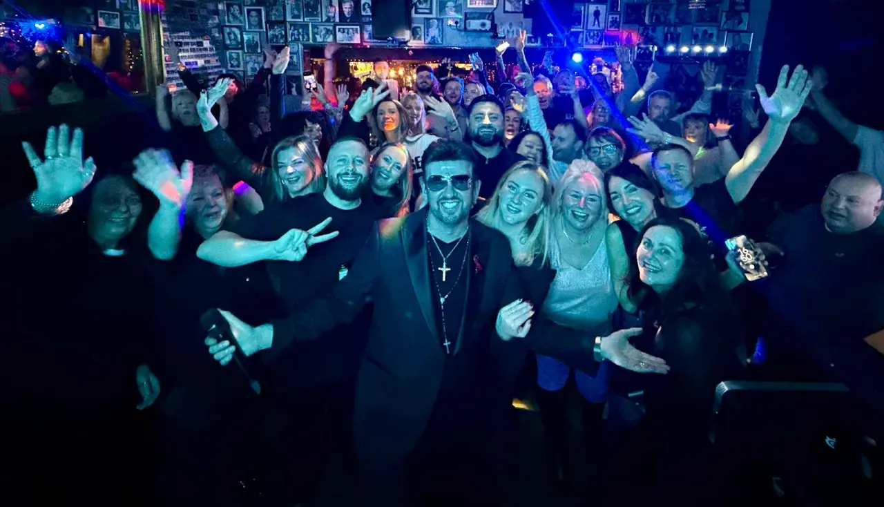 Large crowd of people dancing and celebrating in a nightclub with blue and pink lighting.