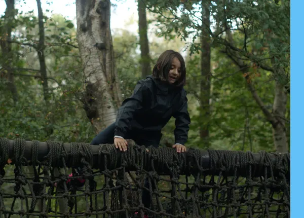 Person balancing on a rope obstacle course in a woodland setting.