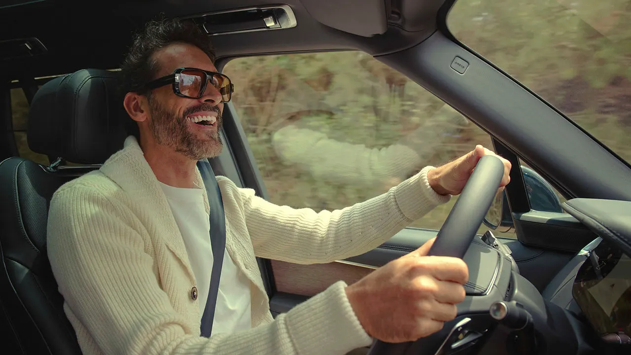 Man smiling while driving a Land Rover vehicle with countryside visible through the windows.