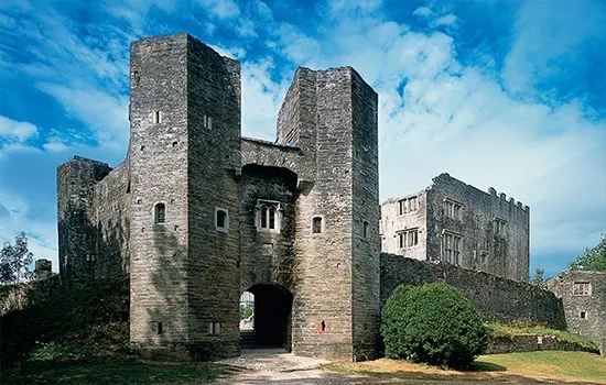 Ruins of a medieval castle gatehouse with twin towers and stone walls under a blue sky.